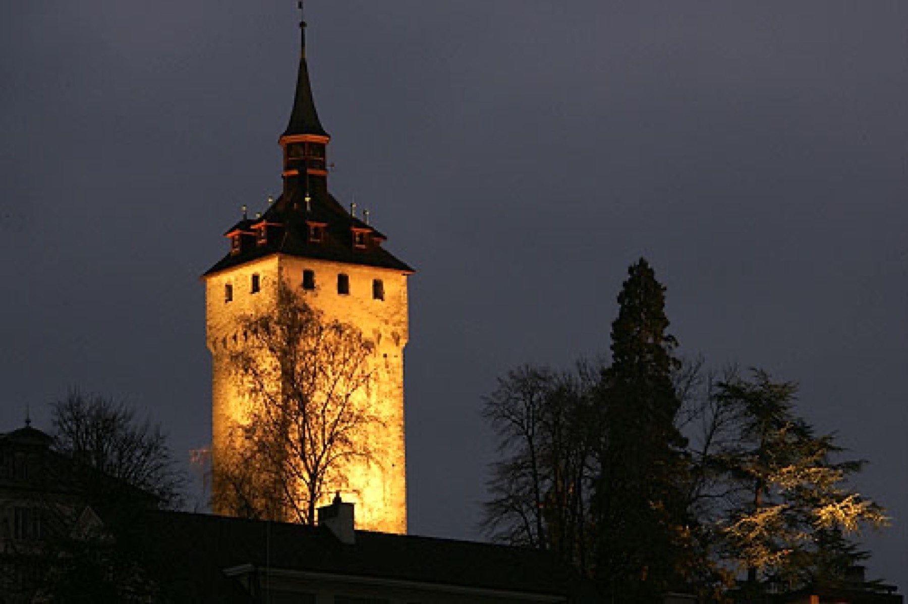 A lit tower of the Musegg Wall above Lucerne at night